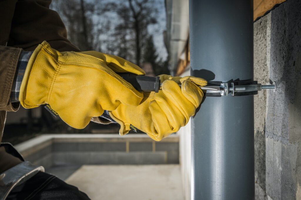 Construction Worker Attaching Home Gutters to the Building Wall